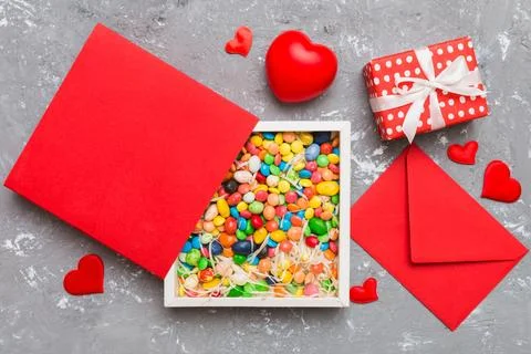 Red envelope with candy and gift box and Valentines hearts on colored backg.. Stock Photos