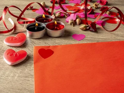 Red envelope next to candles with red rose petals and hearts on the table Stock Photos