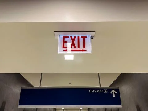 Red exit sign above an elevator sign Stock Photos