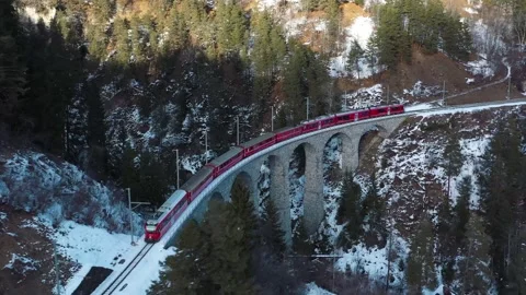 Red express train crossing alpine stone viaduct bridge in snow covered Swis.. Stock Footage 337818257