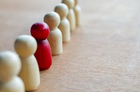 A red figurine being the focus in the queue of wooden dolls. Stock Photos