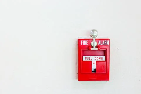 Red fire alarm switch with pull down lever mounted on wall Stock Photos