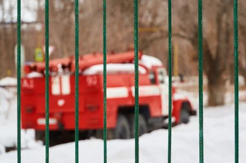 The red fire engine is out of focus behind the iron fence. Stock Photos