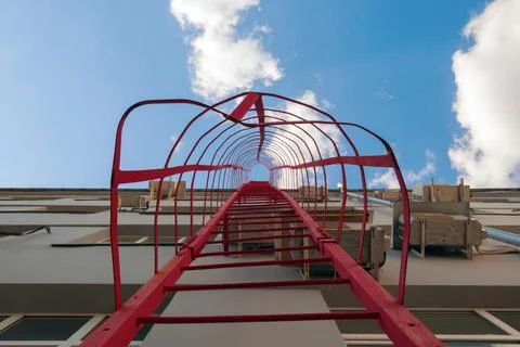 A red fire escape on the facade of a gray building, against a blue sky with Foto stock
