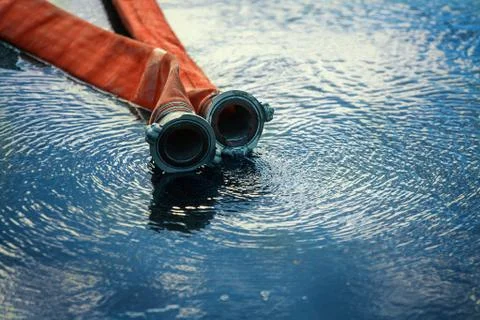 Red fire hose lying in a puddle of water. Fire fighting theme with space to c Stock Photos