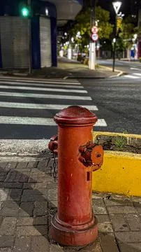 A red fire hydrant on a brick sidewalk, with a pedestrian crossing in the bac Stock Photos