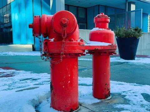 Red fire hydrant on city sidewalk with snow and modern building Stock Photos