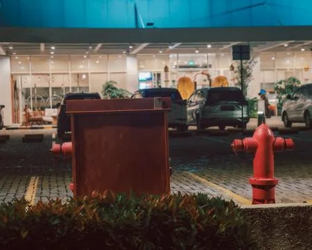 Red fire hydrant in a modern paved parking lot at night with illuminated bui Foto stock
