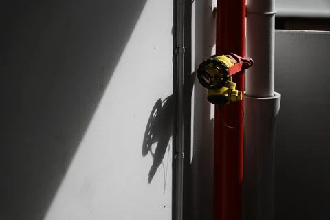 Red fire hydrant pipe with yellow valve in a corner of a building. Stock Photos