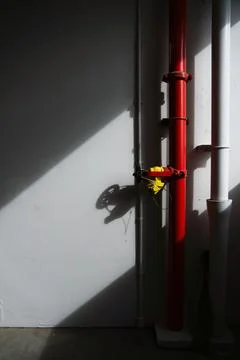 Red fire hydrant pipe with yellow valve on a white wall. Stock Photos