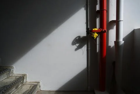 Red fire hydrant pipe with yellow valve on a white wall in a stairwell. Foto stock