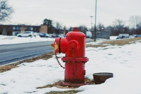 A red fire hydrant is placed on the edge of a snowy area next to a road. Cars Stock Photos