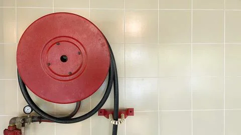 Red fire hydrant reel on a wall waiting for action 스톡 사진