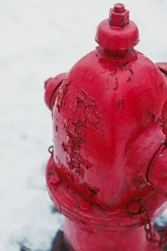 A red fire hydrant shows signs of wear and tear as it sits in the snow. The c Stock Photos