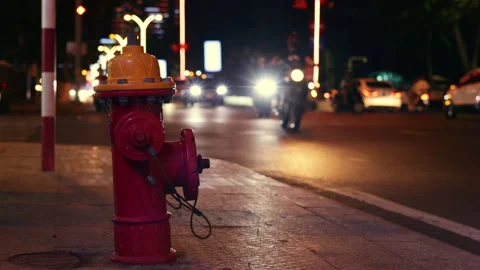 Red fire hydrant on sidewalk with night traffic moving Stock Footage 336099434