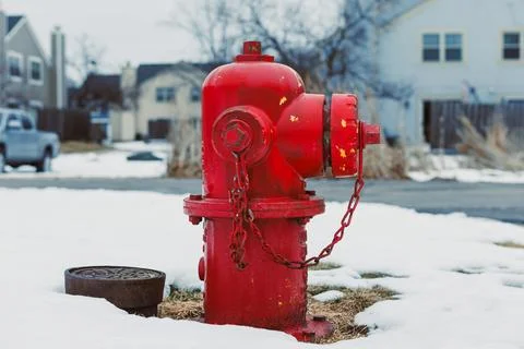 A red fire hydrant sits on a patch of snow with grass peeking through. Nearby Stock Photos