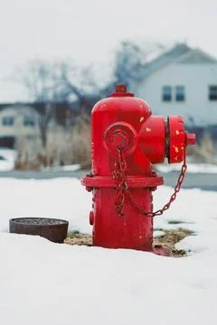 A red fire hydrant sits in the snow near houses, showing its importance for f Stock Photos