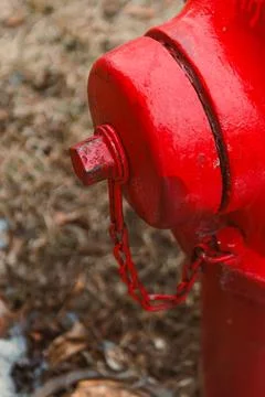 A red fire hydrant stands on the edge of the sidewalk next to brown grass. It Stock Photos