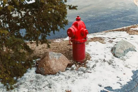 Red fire hydrant stands next to rocks and snow in a winter setting near a r.. Stock Photos