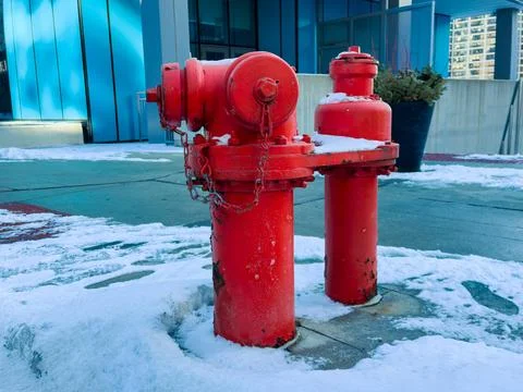 A red fire hydrant stands in the snow beside a building in a city. Snow cover Stock Photos
