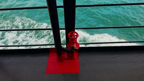 Red Fire Valve Mounted on Ferry Deck Railing With Turquoise Sea and Foamy Water Video stock 328409879