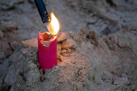 A red firework stuck in the sand is lit with a black stick lighter Foto stock