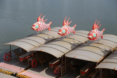 Red fish decorations mounted on covered river boats floating beside calm wate Stock-Fotos