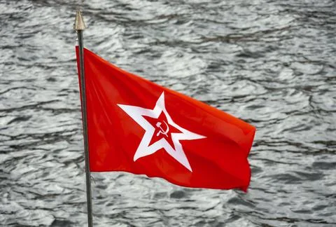 Red flag with five-pointed star and hammer and sickle on background of water. Stock Photos