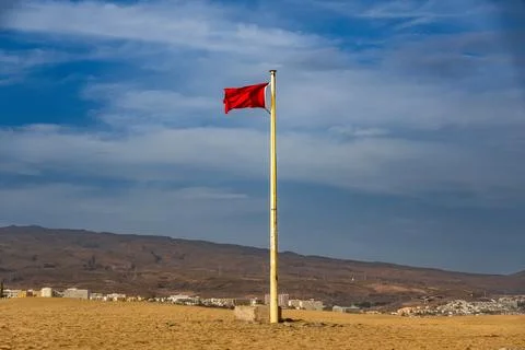 A red flag fluttering in the wind on top of sand dunes, with vast desert Stock Photos