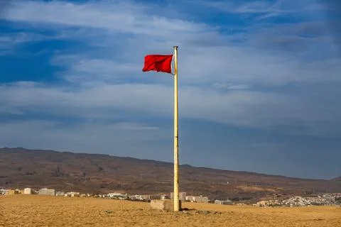 A red flag fluttering in the wind on top of sand dunes, with vast desert Stock Photos