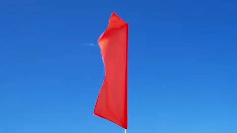 Red flag flutters in wind against sky Stockbeeldmateriaal 342135385