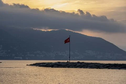 A red flag is flying on a pole in front of a body of water Fotos Stock