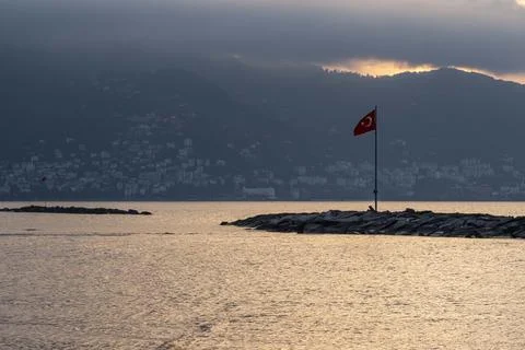 A red flag is flying on a pole in front of a body of water Stock-Fotos