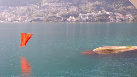 Red flag in front of bulbous bow of a big ship, fluttering above water surface - Stock Footage 231242768