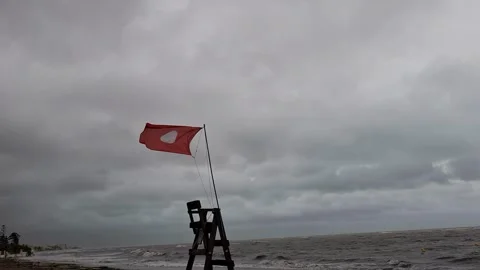A red flag on a lifeguard tower indicating no swimming against a stormy sky  스톡 동영상 337355177