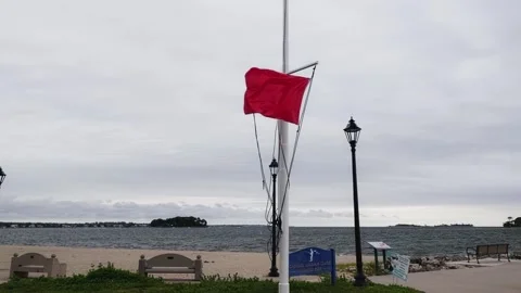 Red flag warning hoisted on a calm overcast day at the beach with benches and la Vídeo Stock 346097624