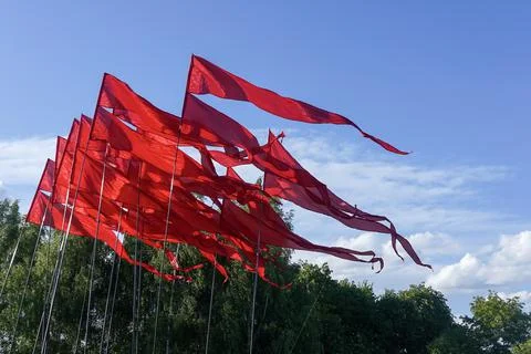 Red flags fluttering in the wind with blue sky and trees in the background Foto stock