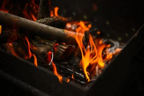 Red flame from a cut of a tree, dark gray coals inside a metal brazier. Firew Stock Photos