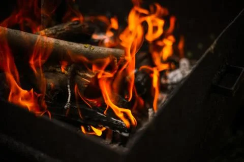 Red flame from a cut of a tree, dark gray coals inside a metal brazier. Firew Stock Photos