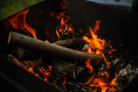 Red flame from a cut of a tree, dark gray coals inside a metal brazier. Firew Stock-Fotos