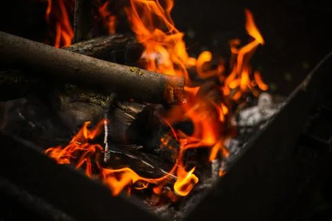 Red flame from a cut of a tree, dark gray coals inside a metal brazier. Firew Stock Photos
