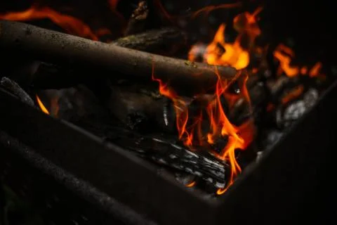 Red flame from a cut of a tree, dark gray coals inside a metal brazier. Firew Stock-Fotos
