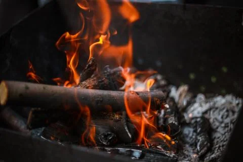 Red flame from a cut of a tree, dark gray coals inside a metal brazier. Firew Stock-Fotos