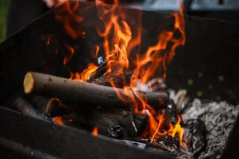Red flame from a cut of a tree, dark gray coals inside a metal brazier. Firew Stock Photos