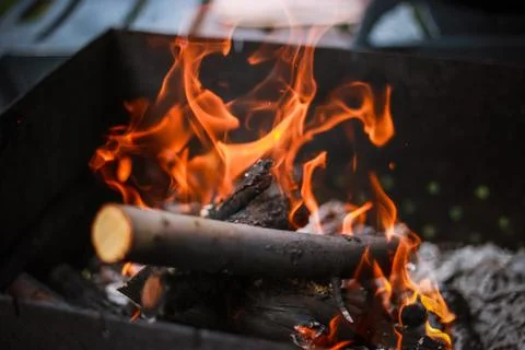 Red flame from a cut of a tree, dark gray coals inside a metal brazier. Firew Stock Photos