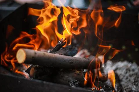 Red flame from a cut of a tree, dark gray coals inside a metal brazier. Firew Stock Photos