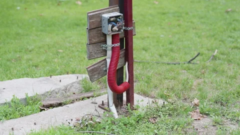 Red flexible hose connected to a utility box on a wooden post, with green grass Stock Footage 340554183