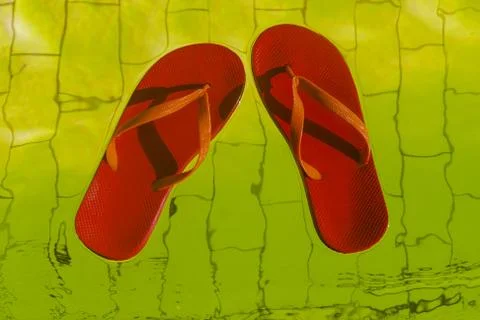 Red flip-flops floating in a pool of yellow water, top view Stock Photos