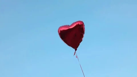 A red foil balloon in the shape of a heart filled with helium flies against t Stock Footage 154369282