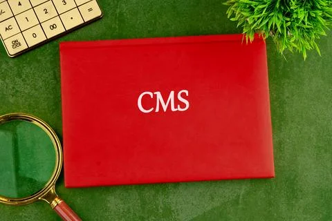 A red folder featuring the abbreviation CMS sits on a green textured surface, Stock Photos